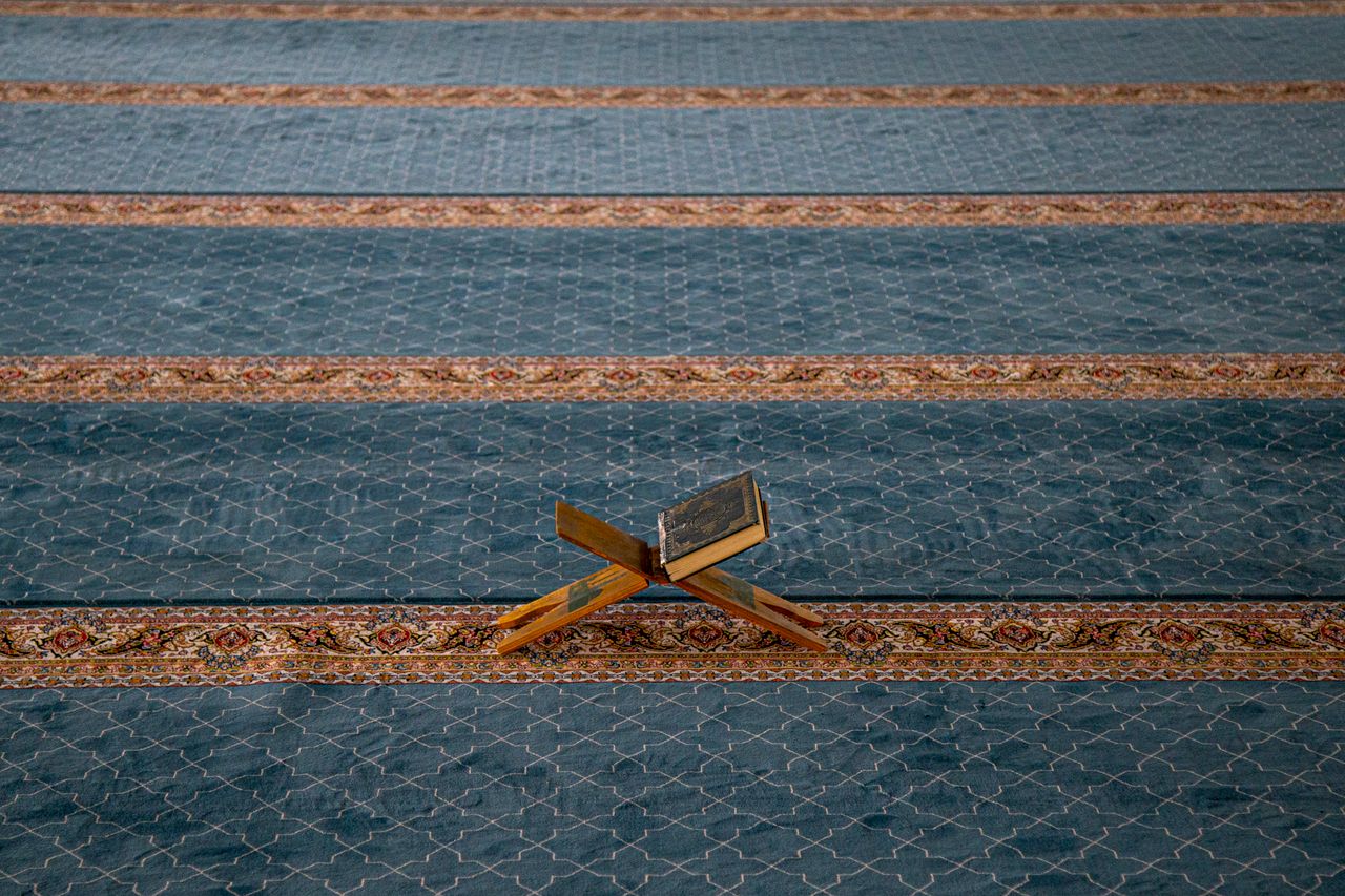 A Quran rests on a wooden stand on patterned carpet, symbolizing Islamic spirituality.